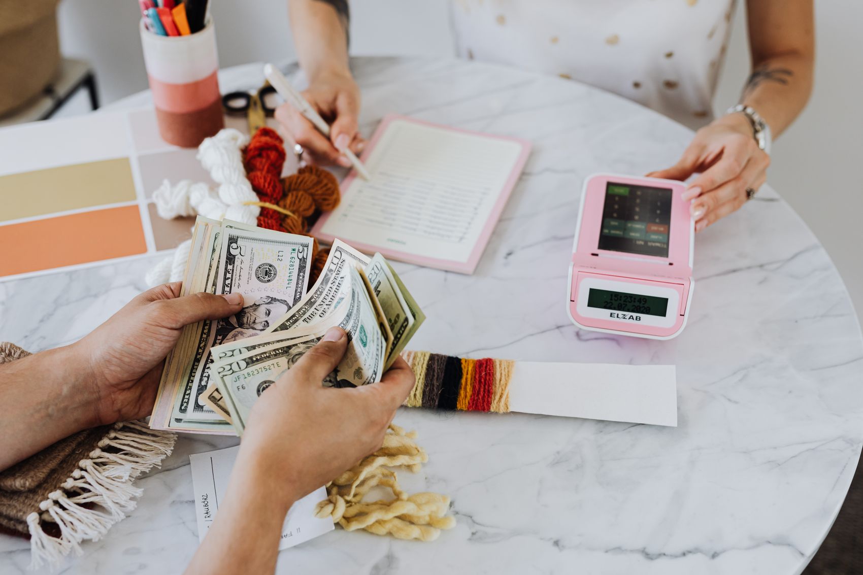 Hands counting donated cash beside a fundraising notebook and card reader