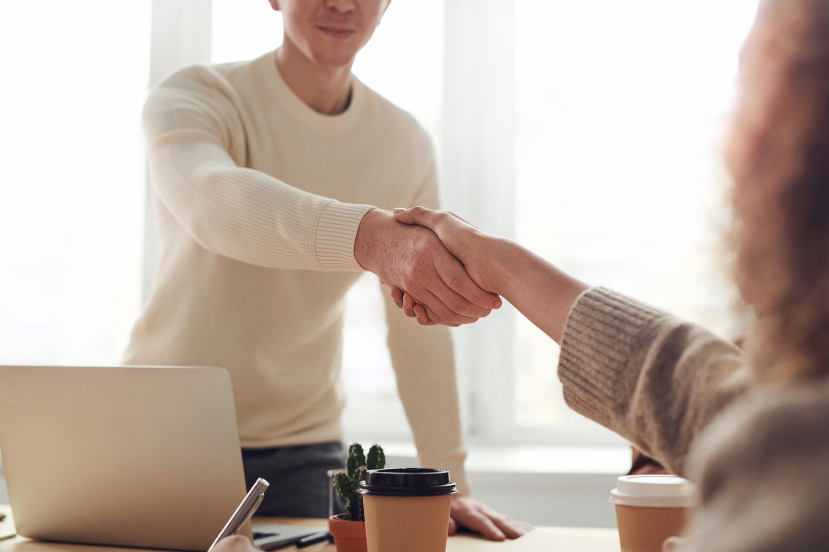 Two people shaking hands over a desk, confirming a fundraising sponsorship or matching gift